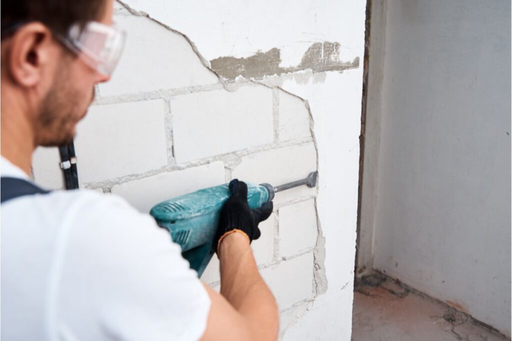 man with demolition hammer removing stucco from wall